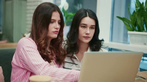 Two Young Women Using a Laptop in a Cafe