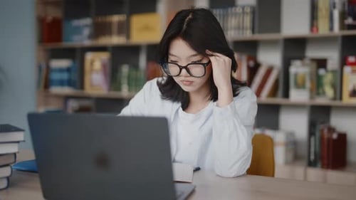 Stressed asian student feeling headache studying in library