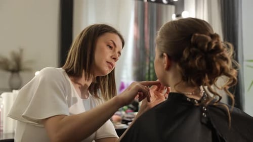 Talented Makeup Artist Meticulously Applies Makeup to a Beautiful Client in a Modern Studio Setting