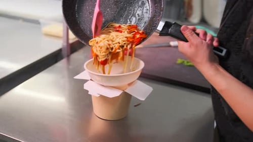 Cook pouring soba udon into paper box wok package for delivery to client, close-up.