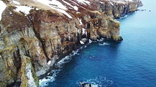 Flying Over Rocky Coastline Cliffside with Snow Over Blue North Atlantic Ocean Water at Spring