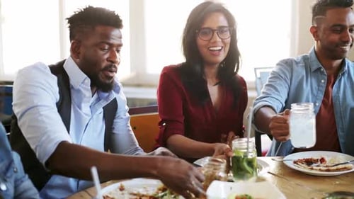 Leisure, Food And People Concept - Group Of Happy International Friends Eating And Clinking Glass...