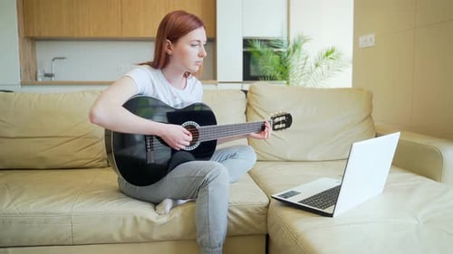 Woman Plays Guitar While Watching Laptop at Home