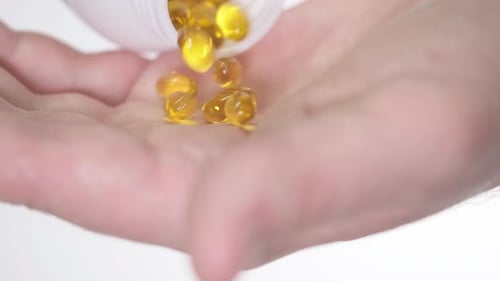Hand Pours Yellow Capsules from Bottle