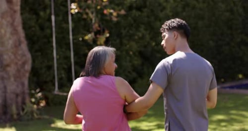 Helping senior woman walk, male physiotherapist supporting her in garden