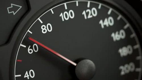 Close-up of a car speedometer showing approximately 60 kmh with a red needle and blurred blue