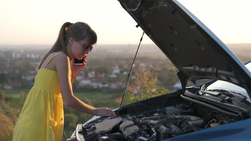Young Woman Driver Talking on Mobile Phone Standing Near Her Car with Open Hood Having Motor Problem