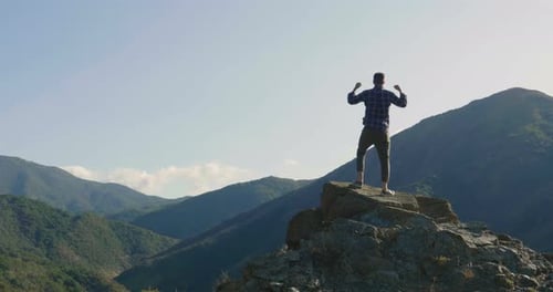 On the edge of a rocky cliff a man raises his hands to heaven as a sign of freedom or victory and