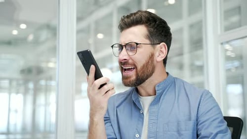 Angry businessman arguing talking on phone sitting at workplace in office. Excited dissatisfied