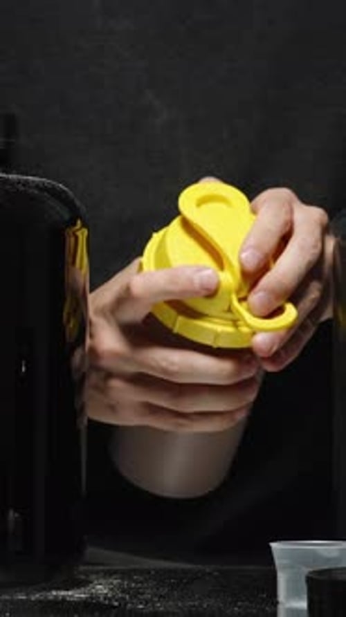 Vertical video. A Man Shakes Chocolate Protein In A Shaker And Tastes It. Next To Him Are Black Cans