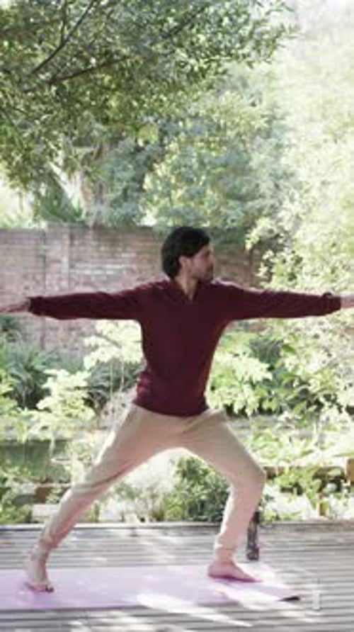 Vertical video of biracial man practicing yoga on sunny terrace, slow motion