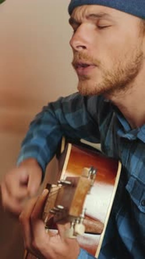 Joyful rock guitarist playing on acoustic guitar and singing. Vertical video