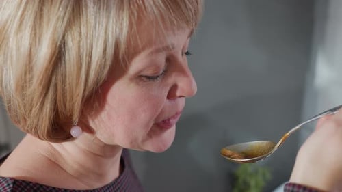 Mature Woman Tasting Food With Spoon in Kitchen