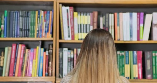 Woman Browsing Books on a Wooden Bookshelf