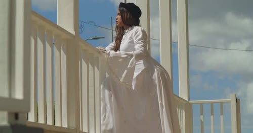 A young lady in a vintage wedding dress leans elegantly on the edge of an old fort.