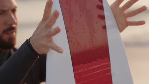 Surfer Checks His Surfboard on the Beach Before Entering the Waves