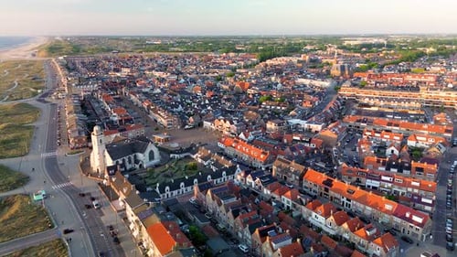 Aerial view of a seaside town at sunset, showing red-roofed houses, a historic church, sandy dunes