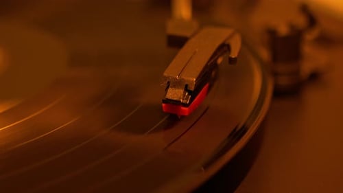 Close-up shot of a vinyl record spinning on a turntable with stylus arm in focus. Vintage analog aud
