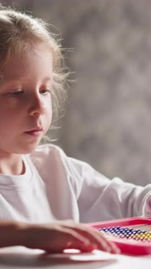 Niña estudiante juega con un ábaco colorido sentado en la mesa