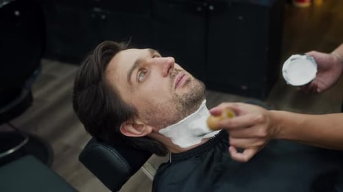 Barbier bereitet Neck of Man auf die Rasur vor, indem er Seifenschaum im Barbershop aufträgt
