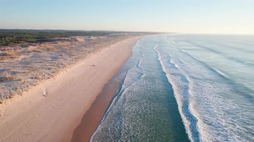 Drone following the coastline along a sandy beach with rolling ocean waves.