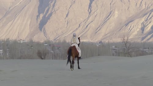 Un cavalier solitaire traverse les vastes dunes de sable du Pakistan avec des montagnes majestueuses à l'horizon