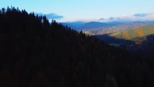 Fast aerial flyover above autumn forest revealing a rural village below colorful hills FHD