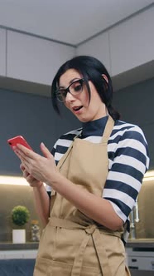 Woman in Apron Looks at Phone and Celebrates