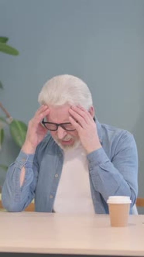 Senior Man Experiencing Headache Pain at Table