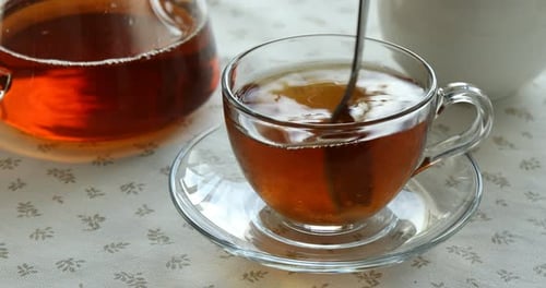 Adding and stirring sugar in cup with aromatic tea at table, closeup