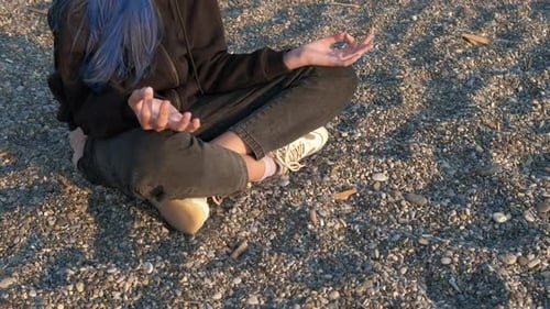 Girl Meditating on Rocky Beach in Sunlight