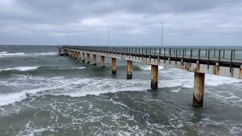 A Pier Extends Into the Ocean As Choppy Waves Hit Its Structure Under Gray Skies The Scene Captures