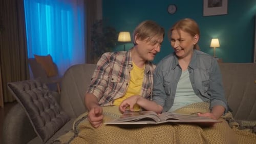 A Married Couple is Looking at a Family Photo Album A Man and a Woman are Sitting on a Couch in the