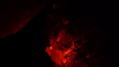 Orange and black glowing embers in a fire with little flames, close up.