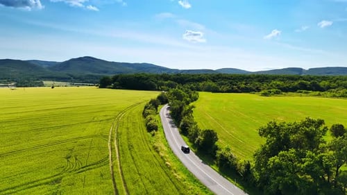 Driving through winding fields. A black car travels down a winding road surrounded