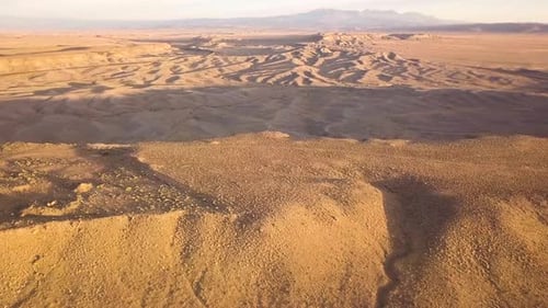 A dolly aerial of a beautiful rocky desert at sunset with sand ripples and harsh shadows.