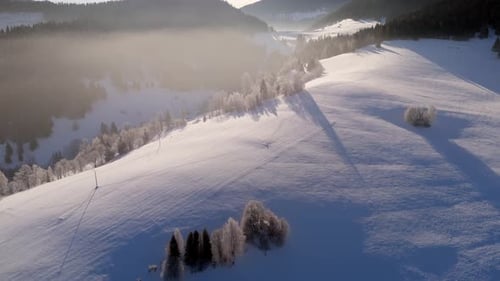 Eine malerische Winterlandschaftsstraße aus der Luft, die sich durch ein nebliges Tal zwischen verschneiten Hügeln schlängelt