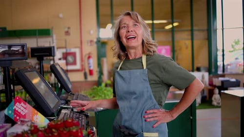 Portrait of a friendly senior female cashier working at a grocery store, smiling and happily giving