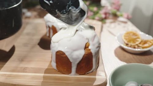Homemade Easter cakes on a sunny table, a woman pouring thick white icing over them.
