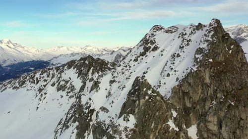 Aerial footage dollying forward towards a snow covered rocky mountain before panning left to reveal