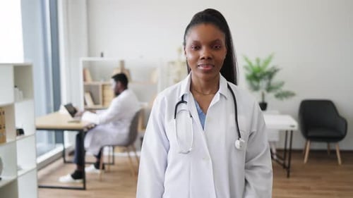 Confident Female Doctor in Office Showing Thumbs Up with Male Colleague Working