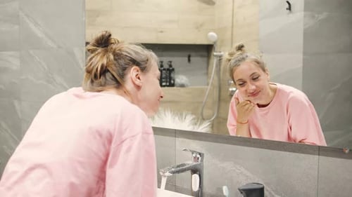 Woman Washing Face and Smiling in Bathroom Mirror
