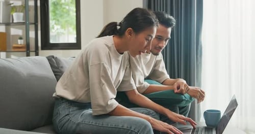 Couple Using Laptop Together on Gray Couch Indoors