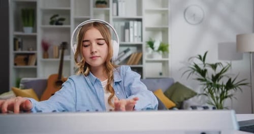 Beautiful preteen girl in headphones playing piano music on synthesizer music studio Music education