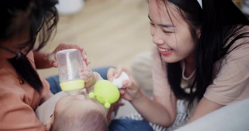 Women Bottle Feeding Baby with Toy Indoors