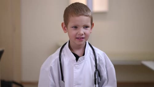 Cute Little Boy in Medical Uniform Looking at Camera and Looking Around Standing in Hospital Indoors