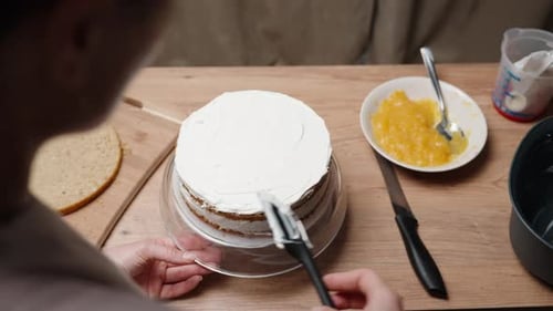 A view from behind the female pastry chef as she finishes covering the sponge cakes with cream
