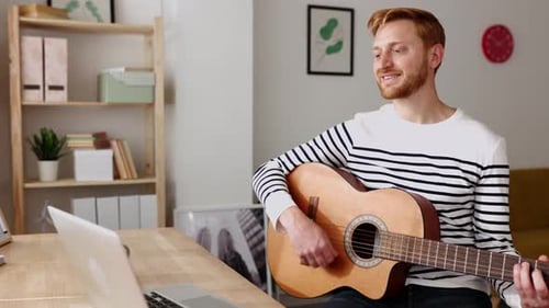 Man Playing Guitar at Desk with Laptop