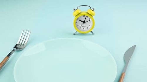 Intermittent fasting, diet, lunch time concept. Alarm clock, plate and cutlery.