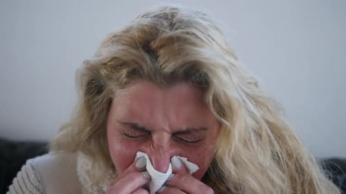 Close-up of a sick woman sneezing into a tissue.